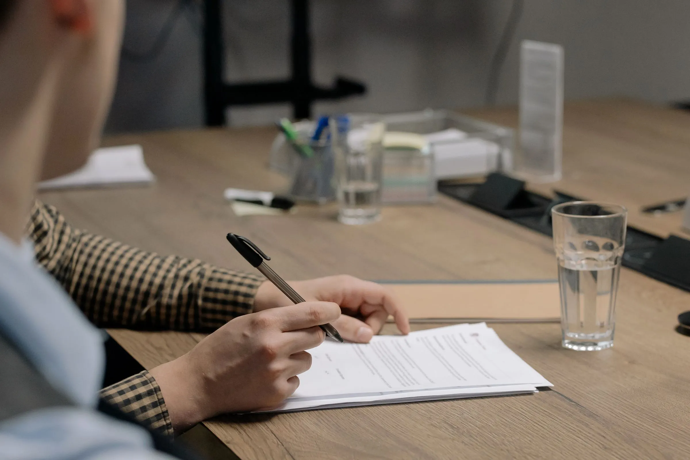 Persona firmando un documento en una mesa de madera.